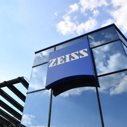 Изображение на модерна стъклена сграда с голямо лого на ZEISS върху нея. 